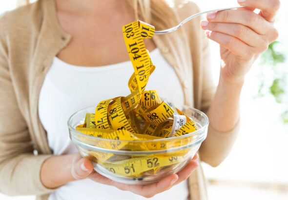 Worried cute woman holding bowl with measuring tapes at home.