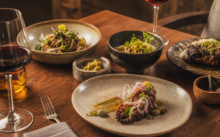 Mesa de cocina mexicana contemporánea con platillos, ingredientes locales y copas de vino.