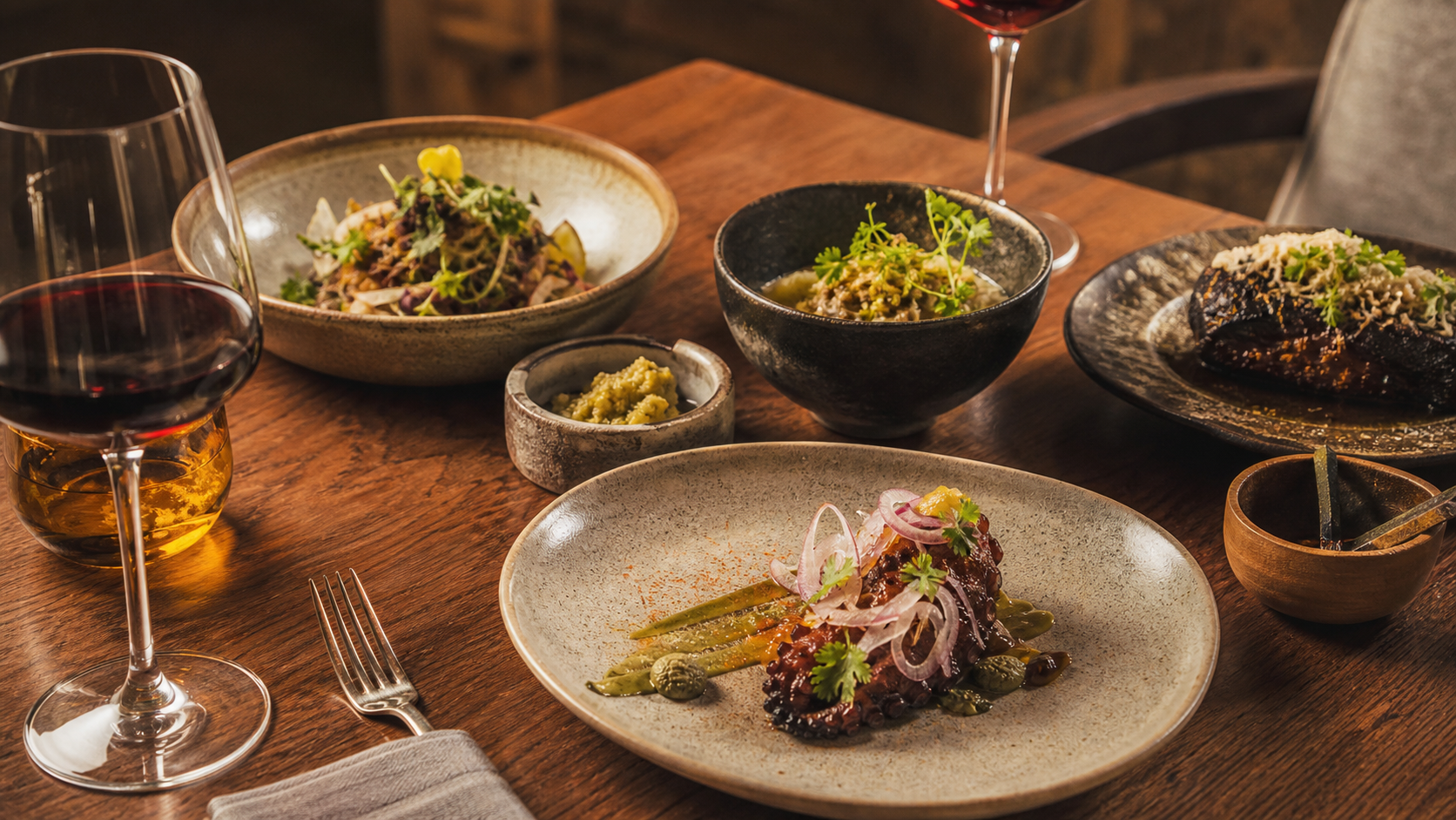 Mesa de cocina mexicana contemporánea con platillos, ingredientes locales y copas de vino.